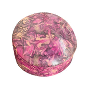 Boîte ronde en cuir marbré rose fuchsia, prune et beige, fermée et vue de trois quarts sur fond blanc.