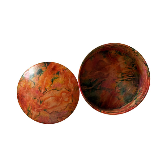 Boîte ronde en cuir marbré corail, orange et vert, ouverte avec son couvercle posé à côté sur fond blanc.