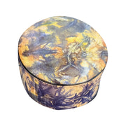 Boîte ronde en cuir marbré violet et jaune ocre, fermée et vue de trois quarts sur fond blanc.