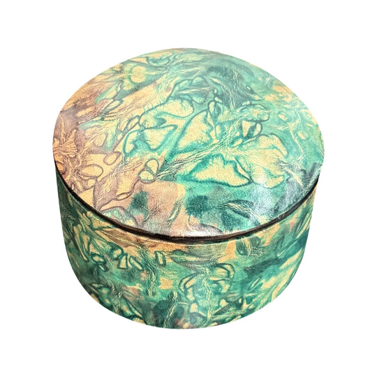 Boîte ronde en cuir marbré vert turquoise et beige, fermée et vue de trois quarts sur fond blanc.