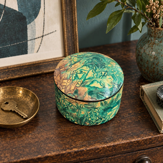 Boîte ronde en cuir marbré vert turquoise et beige, sur une console en bois devant une œuvre encadrée, près d'une coupelle avec une clé.