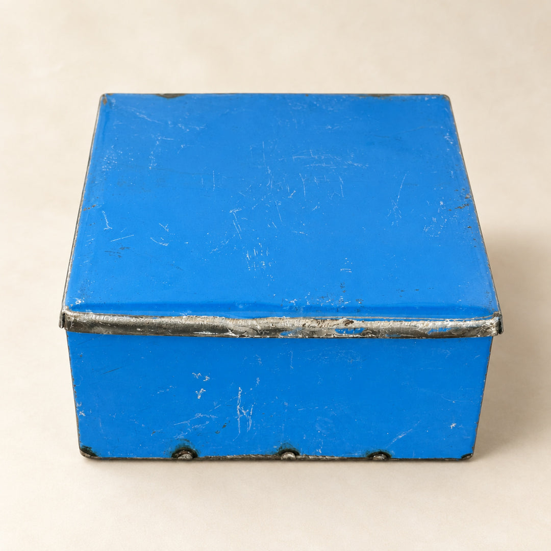 Boîte RANGI bleue fermée sur fond clair, en métal recyclé avec une bordure de couvercle en métal brut.