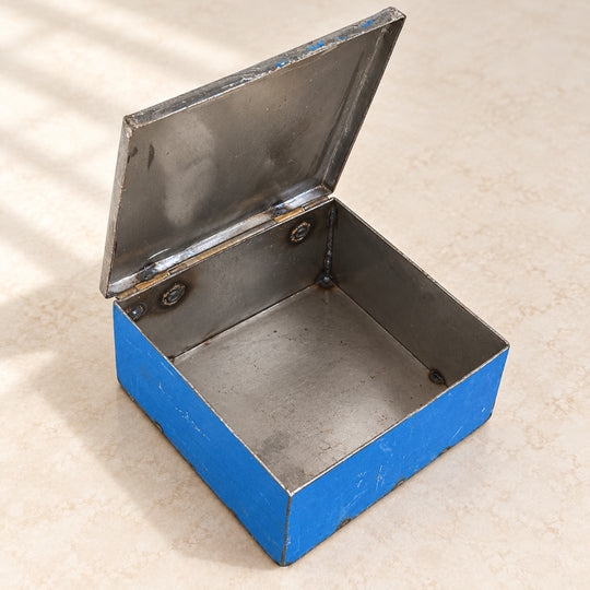 Boîte RANGI bleue ouverte sur fond clair, montrant son intérieur en métal brut et son couvercle relevé.