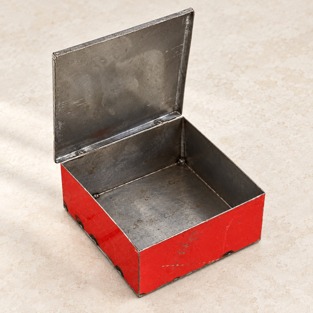 Boîte RANGI rouge ouverte sur fond clair, montrant son intérieur en métal brut et son couvercle relevé.