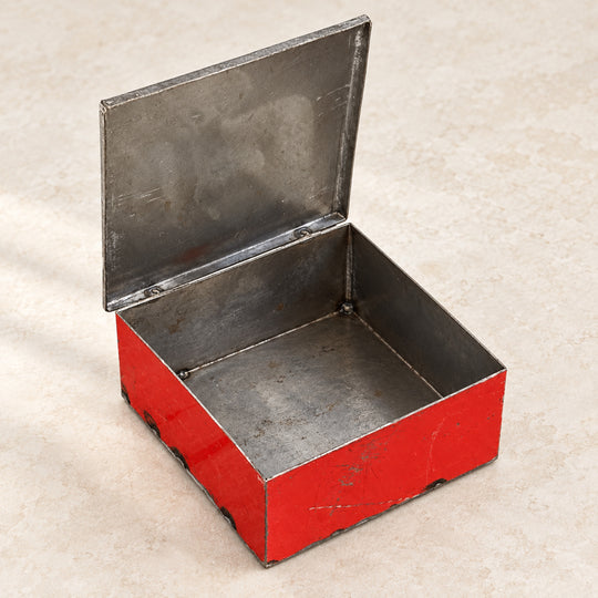 Boîte RANGI rouge ouverte sur fond clair, montrant son intérieur en métal brut et son couvercle relevé.