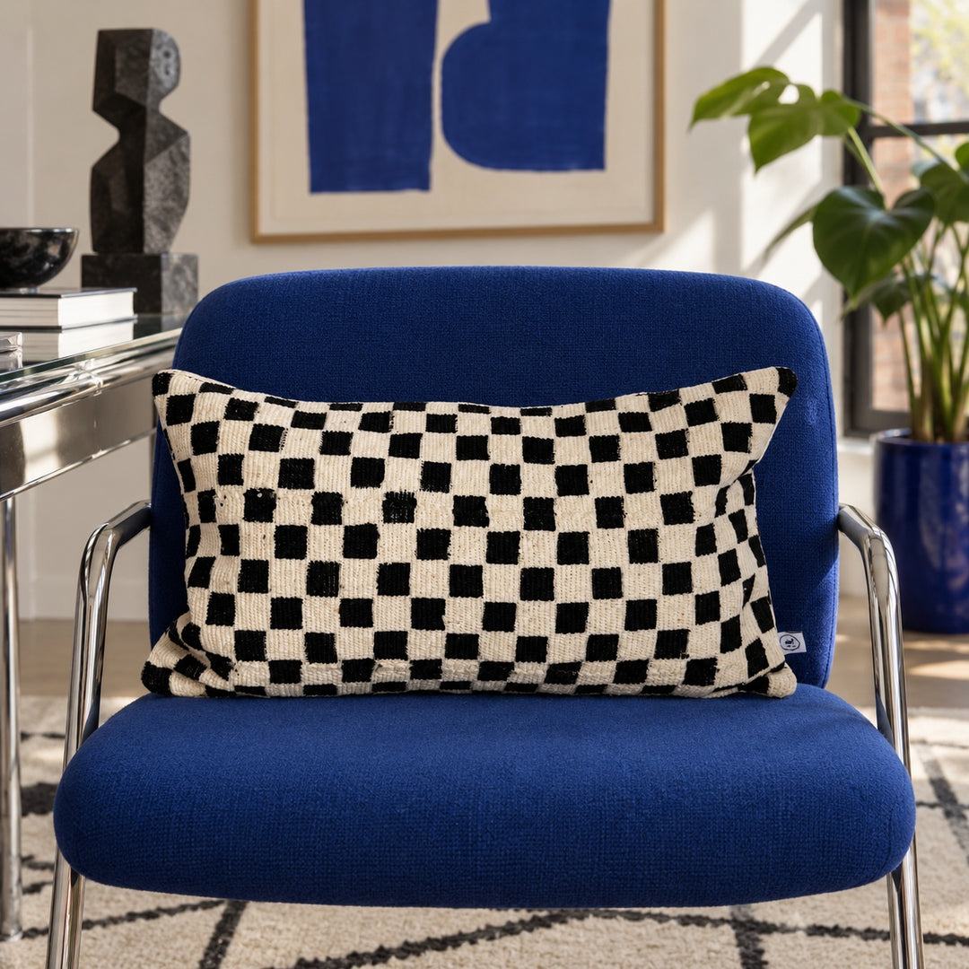 Weißes TANDA Kissen mit schwarzem Schachbrettmuster auf einem blauen Sessel im Arbeitszimmer.